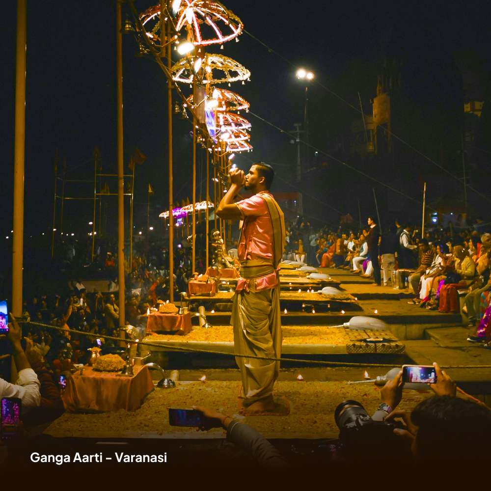 Ganga Aarti ceremony in Varanasi with a man performing and people taking photos.